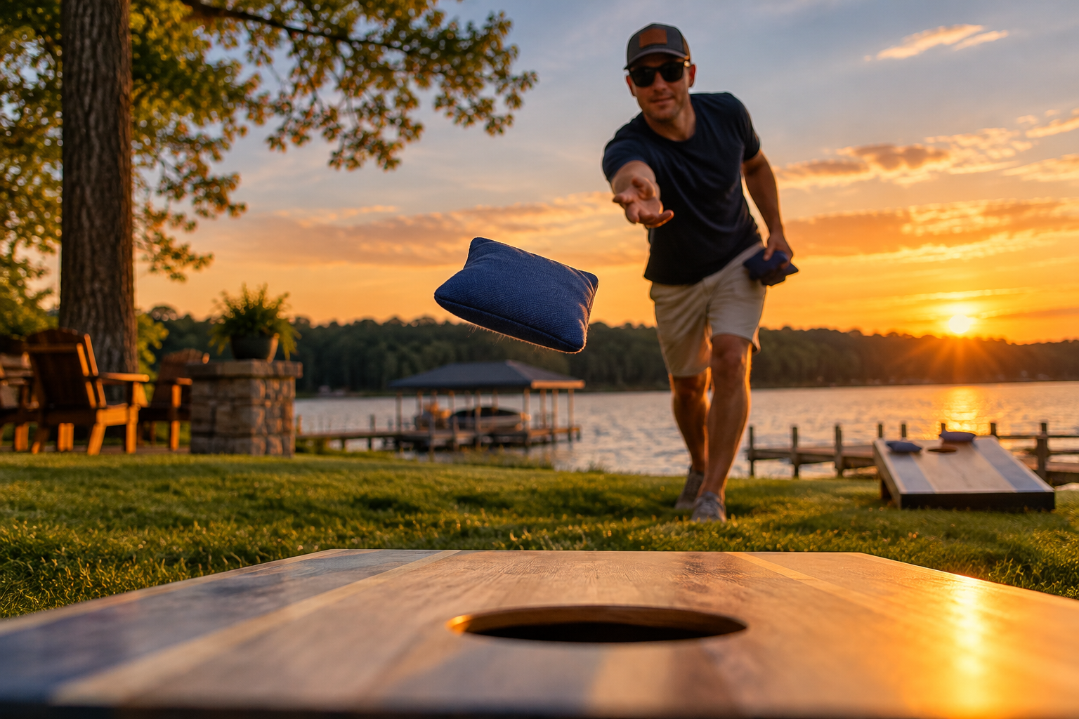 Player throwing a blue cornhole bag toward a wooden board beside a lake at sunset